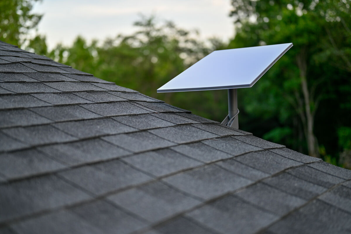 A Starlink satellite dish mounted on a house roof with trees behind, rural broadband for South Taranaki