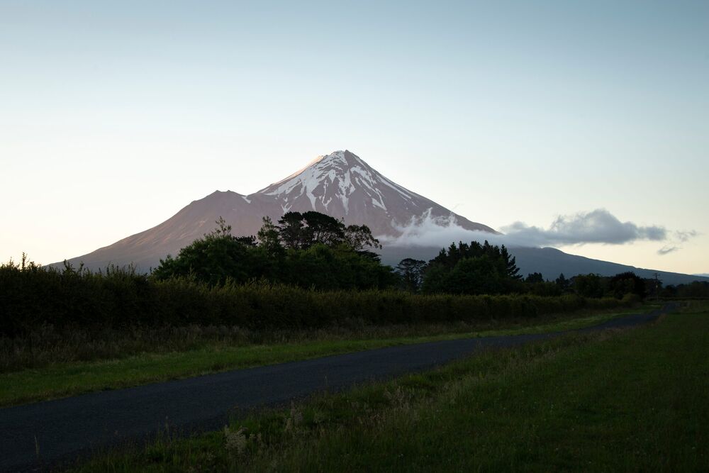 Snow-capped Mount Taranaki at dusk above farmland and a country road, South Taranaki